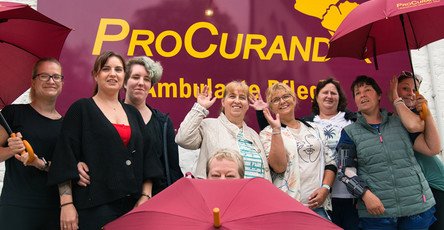 Das Team der ProCurand Ambulanten Pflege Ludwigsfelde steht mit Regenschirmen vor der Einrichtung – gut gelaunt und bereit für einen gemeinsamen Ausflug zum Sound City Festival.