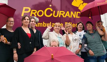 Das Team der ProCurand Ambulanten Pflege Ludwigsfelde steht mit Regenschirmen vor der Einrichtung – gut gelaunt und bereit für einen gemeinsamen Ausflug zum Sound City Festival.