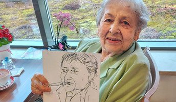 Eine Seniorin der ProCurand Seniorenresidenz Havelpalais hält stolz die Zeichnung, die für sie angefertigt wurde, in die Kamera.