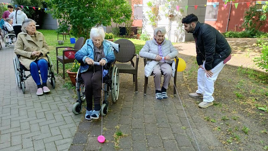 Im Garten der ProCurand Seniorenresidenz Havelpalais ziehen zwei Seniorinnen beim Spiel „Enten aufwickeln“ mit viel Geschick die Bälle an einem Seil zu sich.