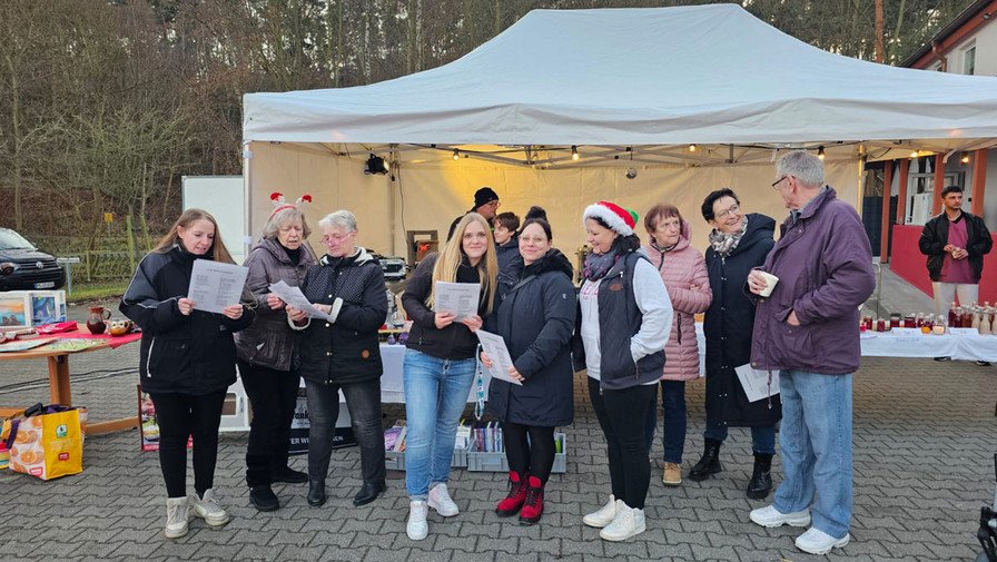 Weihnachtsmarkt vor der ProCurand Seniorenresidenz Am Görnsee in Grebs mit Bewohnerinnen, Angehörigen und Nachbarinnen. DJ Percy Assmann spielt, das Team singt Weihnachtslieder und alle genießen Leckereien wie Kuchen, Glühwein und Waffeln.