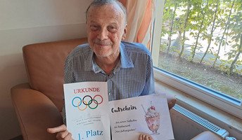 Die Gewinner der Sommer-Ball-Olympiade in der Seniorenresidenz Bölschestraße freuen sich über ihre Urkunden und Eisgutscheine. Stolz haltet einer der Gewinner seinen Preis in die Kamera!