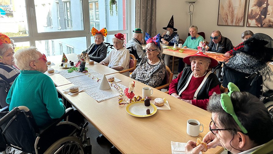 Die Bewohner*innen des ProCurand Pflegestifts Pfarrer Lukas sitzen gemeinsam am Tisch und teilen ihre Glücksmomente während der Faschingsfeier.