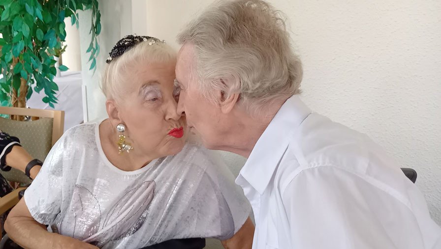 Das Ehepaar Riebisch küsst sich während des Grillfests in der ProCurand Seniorenresidenz Am Straussee und genießt die ausgelassene Stimmung.