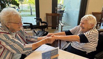 Zwei Seniorinnen der ProCurand Seniorenresidenz Bölschestraße halten sich an den Händen und haben beim Tanztee sichtbar Freude.