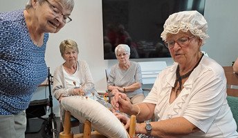 In der ProCurand Residenz Am Hallorenring zeigt Mieterin Monika Hennig konzentriert ihr Klöppel-Hobby, während die anderen Senior*innen gespannt zuschauen und jede Bewegung aufmerksam verfolgen. Die Begeisterung ist deutlich spürbar.