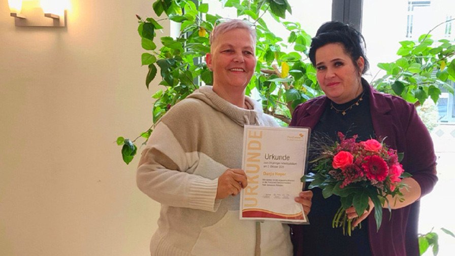 In der ProCurand Seniorenresidenz Park Sanssouci überreicht Pflegedienstleitung Manuela Grund ihrer Kollegin Dunja Hoyer zum 20-jährigen Dienstjubiläum eine Urkunde und einen Blumenstrauß.