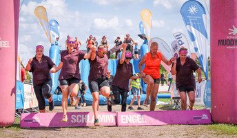 Die Power-Ladies aus der stationären Pflege der ProCurand Seniorenresidenz Am Straussee laufen Hand in Hand lachend über die Ziellinie – voller Schlamm, aber sichtlich stolz.