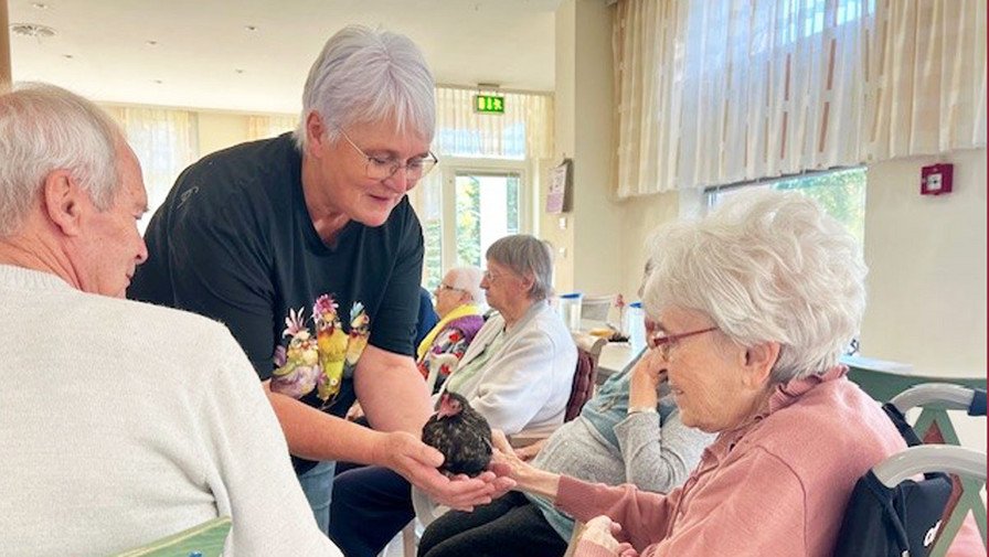In der ProCurand Seniorenresidenz Senftenberg wird ein Therapiehuhn gezeigt, während die Senior*innen interessiert zusehen und den besonderen Moment genießen.