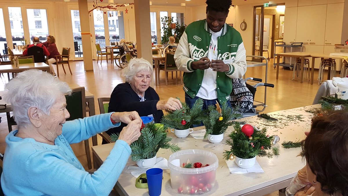 In der ProCurand Seniorenresidenz Bölschestraße basteln mehrere Bewohner*innen gemeinsam Adventsgestecke. Ein Mitarbeiter der sozialen Betreuung unterstützt die Runde.