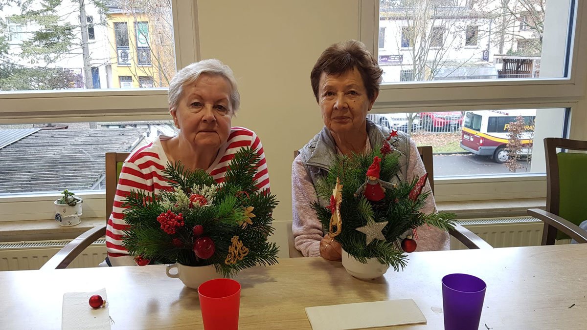 In der ProCurand Seniorenresidenz Bölschestraße sitzen zwei Bewohnerinnen an einem Tisch und gestalten gemeinsam weihnachtliche Adventsdekoration.