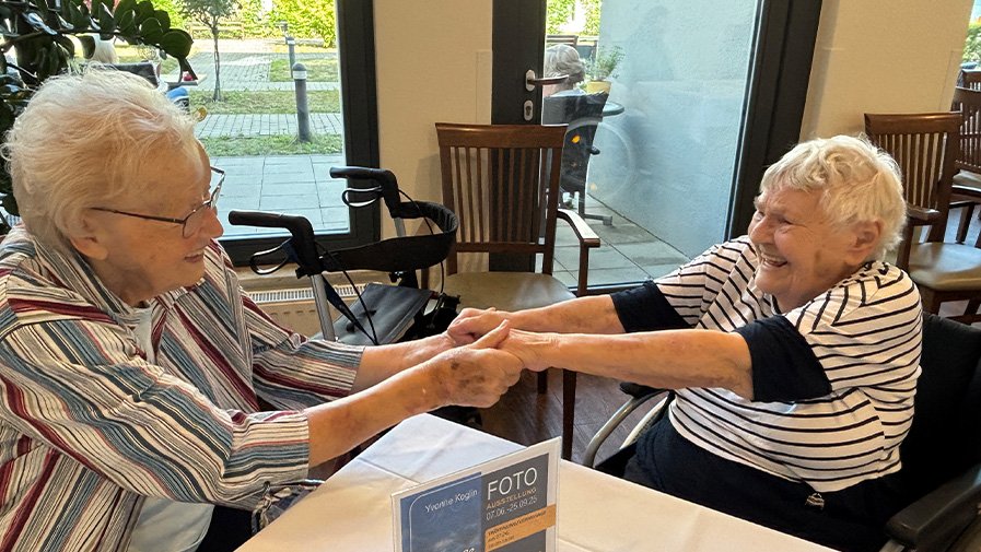 Zwei Seniorinnen der ProCurand Seniorenresidenz Bölschestraße halten sich an den Händen und haben beim Tanztee sichtbar Freude.