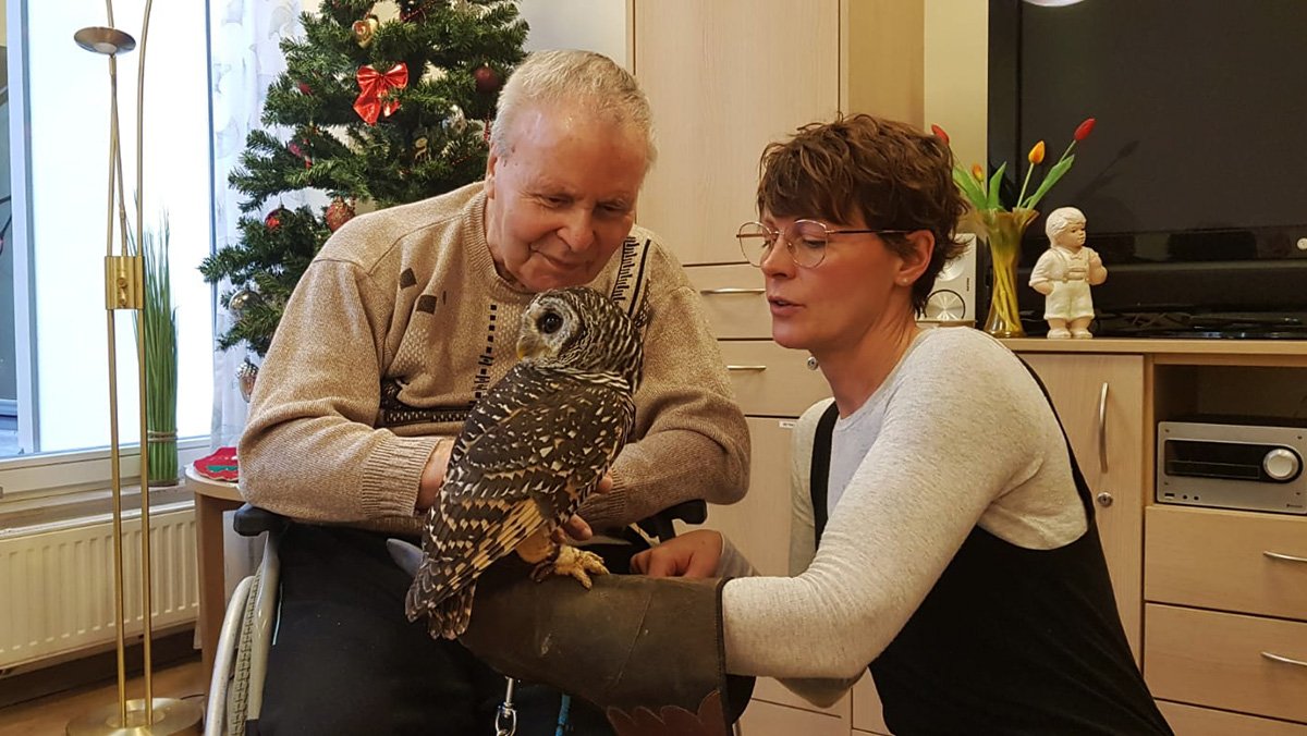 Ein Bewohner der ProCurand Seniorenresidenz Bölschestraße hält mit Unterstützung von Denise Grytzka (Sozialdienst) eine Eule auf dem Arm.
