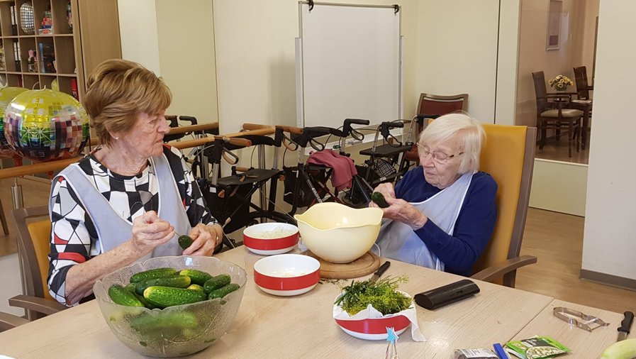 Zwei Bewohnerinnen der ProCurand Seniorenresidenz Bölschestraße bereiten gemeinsam in der Küche Gurken und Gemüse zum Einlegen vor.