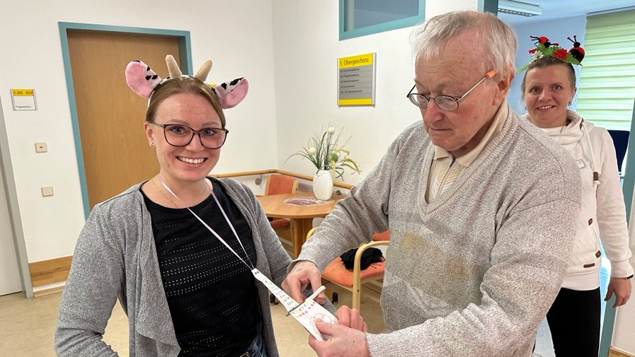 Ein Bewohner des  ProCurand Pflegestift Pfarrer Lukas schneidet die selbstgebastelte Krawatte von Einrichtungsleitung Laura Hewel ab.