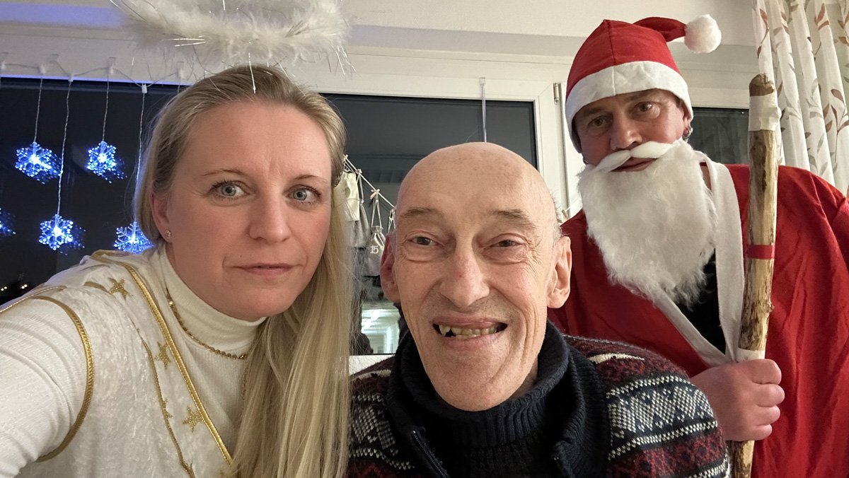 Im ProCurand Pflegestift Pfarrer Lukas in Cham stehen Nikolaus Christian Jaslovsky und Christkind Nicole Roith gemeinsam mit einem Bewohner und überbringen die gefüllten Stiefel.