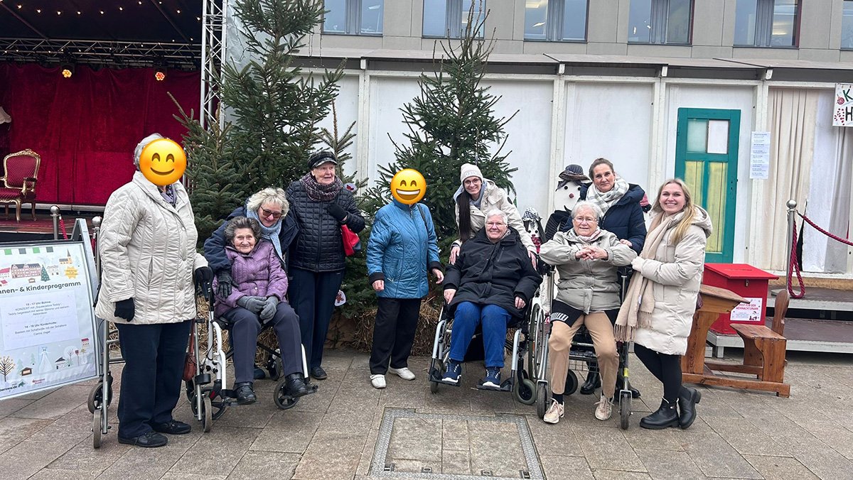 Gäste der ProCurand Tagespflege Eberswalde stehen und sitzen gemeinsam vor einem Weihnachtsbaum auf dem Eberswalder Weihnachtsmarkt.
