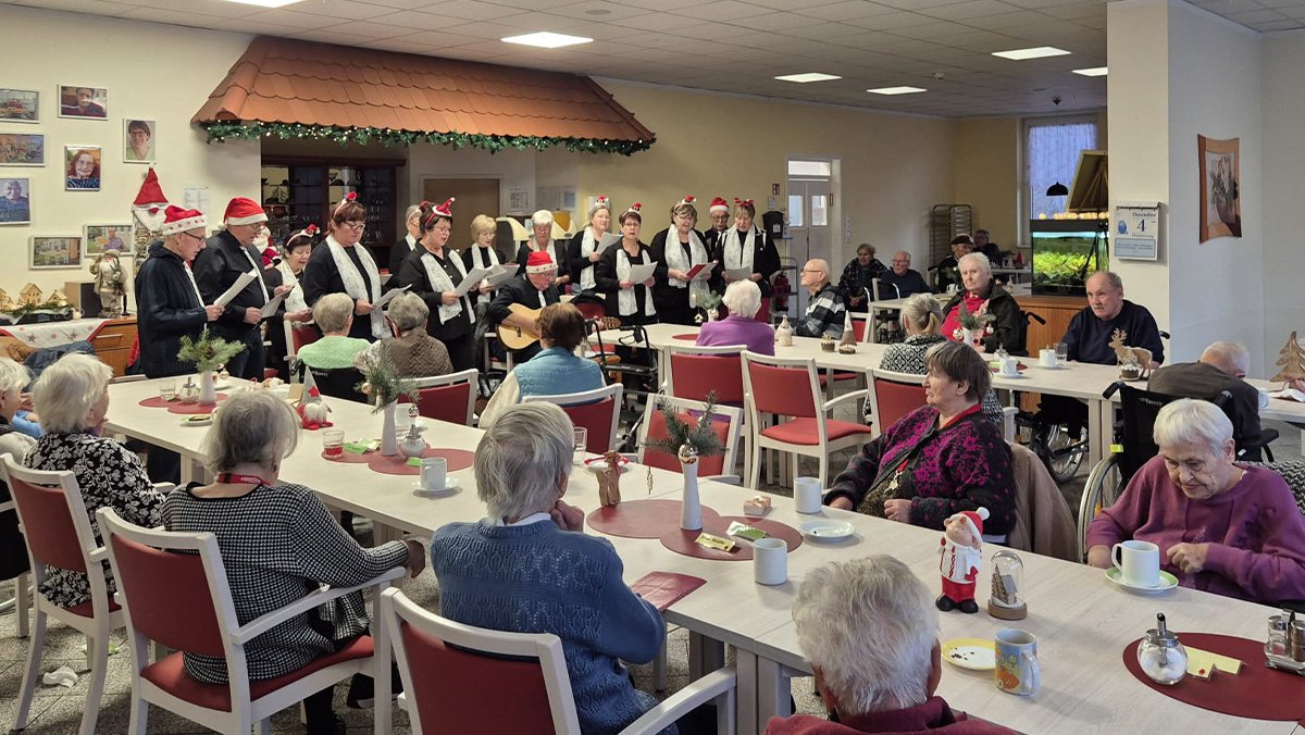 Der Damsdorfer Chor tritt im Gemeinschaftsraum der ProCurand Seniorenresidenz Am Görnsee auf, während die Bewohner*innen an den Tischen zuhören.