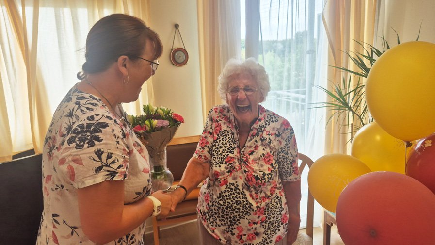 Hildegard Körner empfängt strahlend Blumen von Einrichtungsleitung Ute Knauth in der ProCurand Seniorenresidenz Am Hufeisensee in Halle.