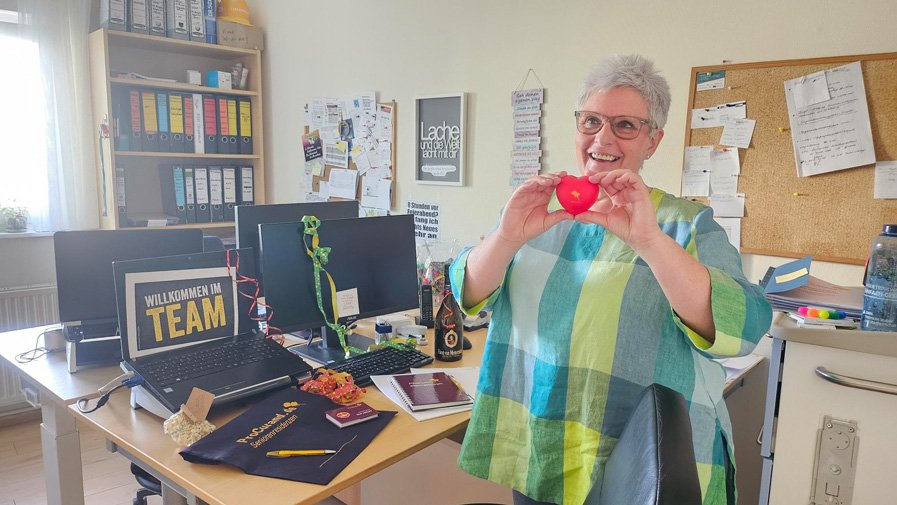 In der ProCurand Seniorenresidenz Am Hufeisensee zeigt sich die neue Ausbildungskoordinatorin Heike Mellmann im Büro mit dem ProCurand-Herz, bereit für ihre neue Aufgabe.