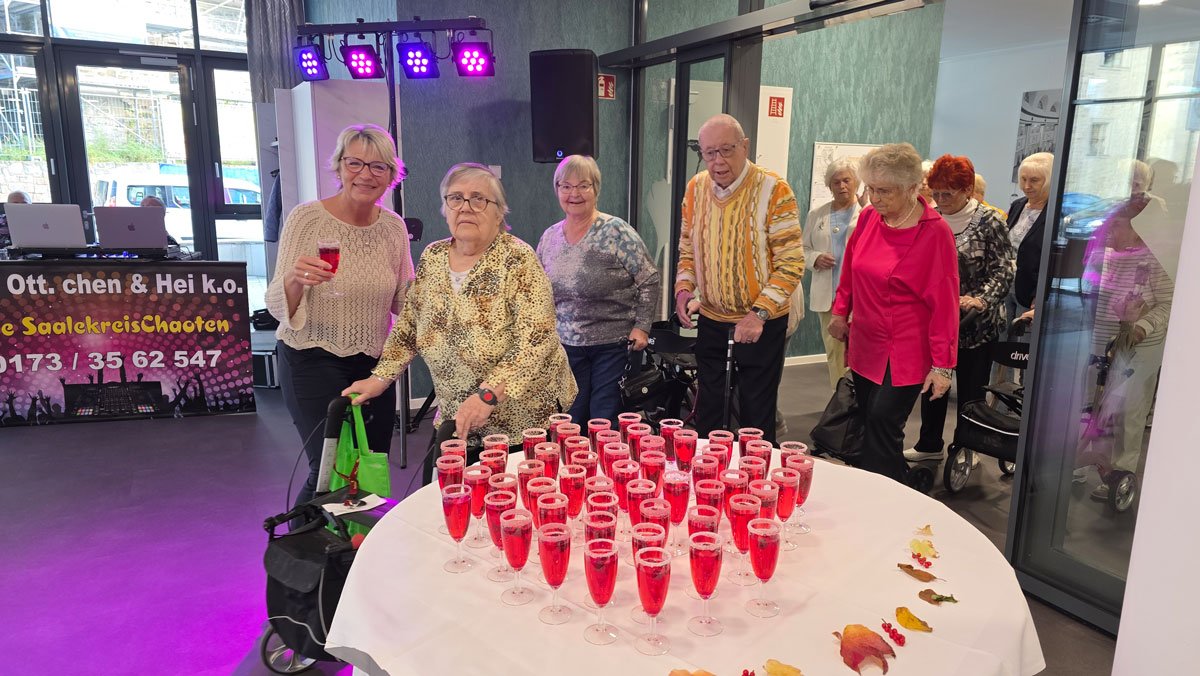 In der ProCurand Seniorenresidenz Am Hallorenring feiern Bewohner*innen zusammen mit der Residenzleitung Melanie End fröhlich zusammen, umgeben von bunter Beleuchtung und festlicher Stimmung.