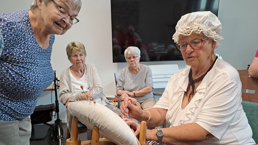 In der ProCurand Residenz Am Hallorenring zeigt Mieterin Monika Hennig konzentriert ihr Klöppel-Hobby, während die anderen Senior*innen gespannt zuschauen und jede Bewegung aufmerksam verfolgen. Die Begeisterung ist deutlich spürbar.