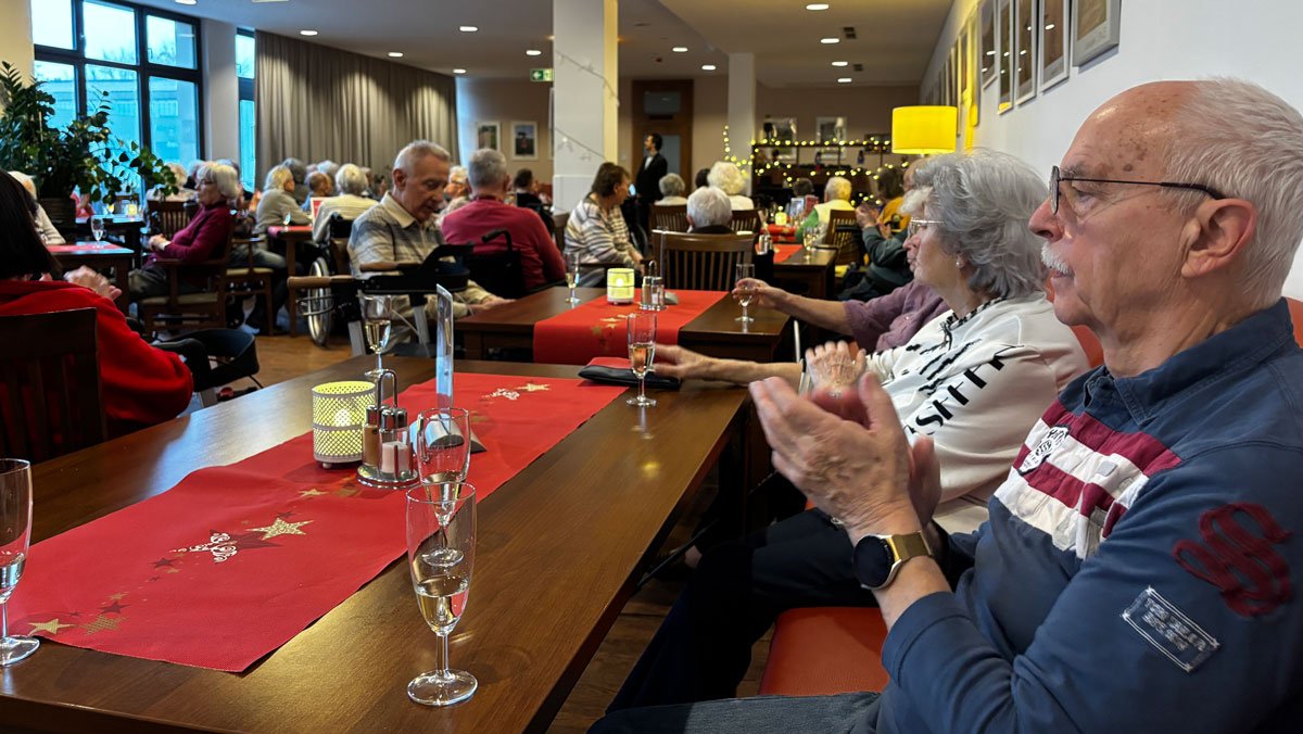 Bewohner*innen der ProCurand Seniorenresidenz Bölschestraße klatschen beim Neujahrsempfang gemeinsam mit einem Glas Sekt auf das neue Jahr an.