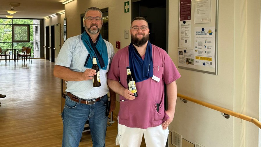 Einrichtungsleiter Enrico Hennig (links) und Mitarbeiter Patrick (rechts) halten kühle Getränke in der Hand, um das Team der ProCurand Seniorenresidenz Havelpalais an heißen Tagen zu erfrischen.