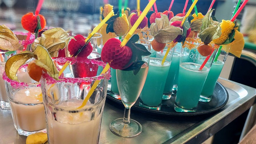 Zahlreiche bunt dekorierte Cocktails – darunter Swimming Pool, Sex on the Beach und Pina Colada – stehen auf Servierplatten bereit, liebevoll arrangiert vom Team Betreuung.