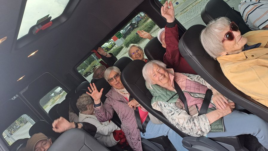 Die Gäste der ProCurand Tagespflege Strausberg sitzen gut gelaunt im Kleinbus nach Oderberg, lachen und heben voller Freude die Hände in die Luft.