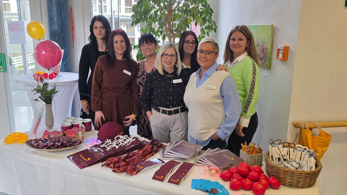 Im Eingangsbereich der ProCurand Seniorenwohnanlage Fideliswiesen stehen sieben Kolleginnen, darunter das Leitungsteam, hinter einem Infotisch mit Materialien und Give-aways.