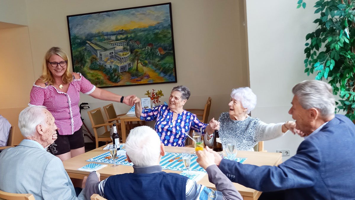 In der ProCurand Seniorenresidenz Am Straussee sitzen Bewohner*innen gemütlich zusammen, unterhalten sich und genießen Getränke, begleitet von herzlicher Betreuung und fröhlicher Stimmung.
