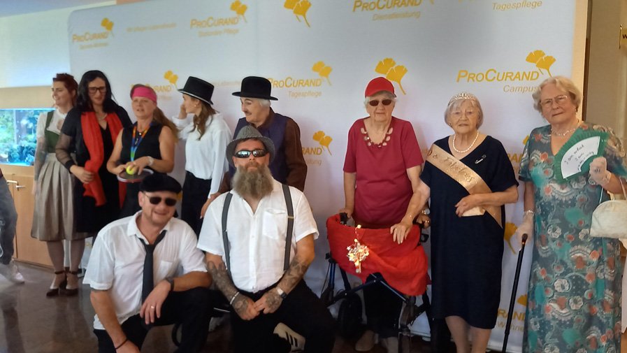 Bewohner*innen und Mitarbeitende der ProCurand Seniorenresidenz Am Straussee posieren kostümiert auf dem roten Teppich, die Stimmung ist ausgelassen und festlich.
