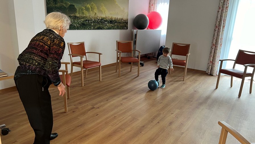 Am Standort Strausberg spielt eine Seniorin mit einem der Kinder Fußball – Generationen begegnen sich mit Freude und Bewegung.