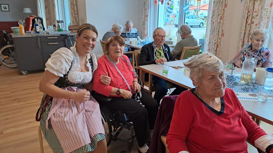 Eine Mitarbeiterin in Dirndl hat viel Spaß mit den Bewohner*innen während des Oktoberfests in der ProCurand Tagespflege Strausberg und sorgt für ausgelassene Stimmung.