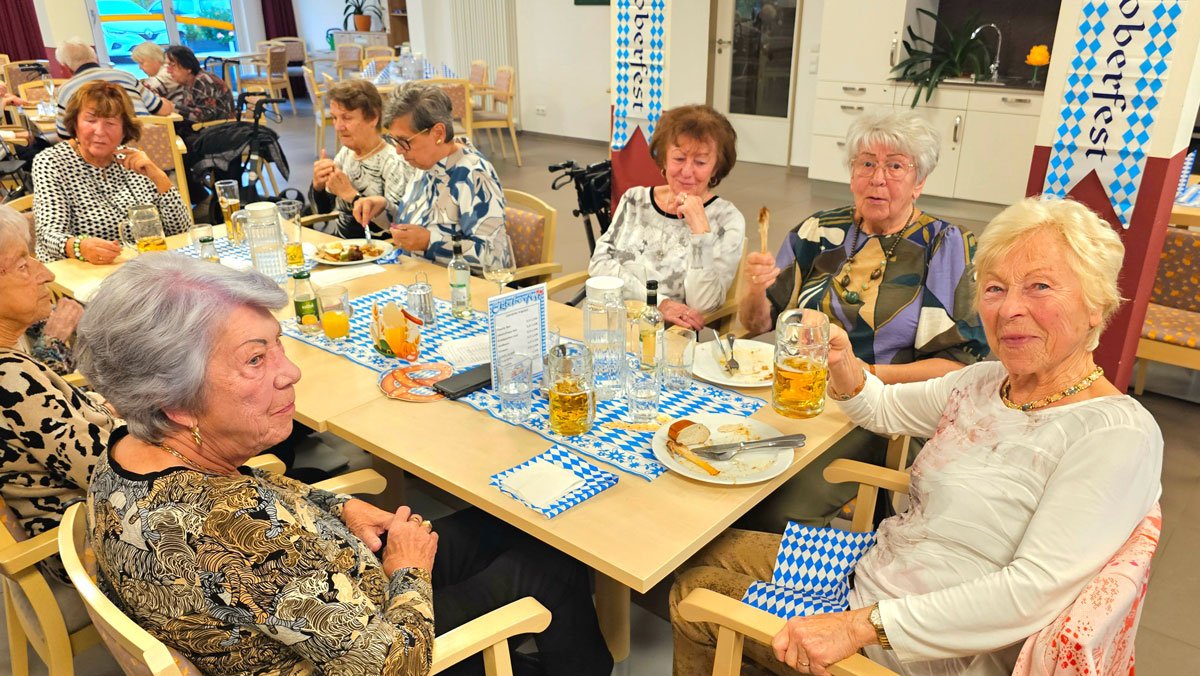 Mieter*innen des ProCurand Service-Wohnen Wriezener Straße genießen in bayerisch dekorierter Atmosphäre gemeinsam Speisen und Getränke.