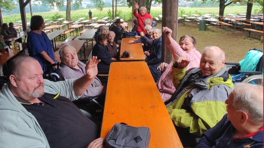 An einem der Tische auf dem Annaberg sitzen die Senior*innen gemütlich zusammen, einige heben die Hände voller Vorfreude auf das bevorstehende Essen.