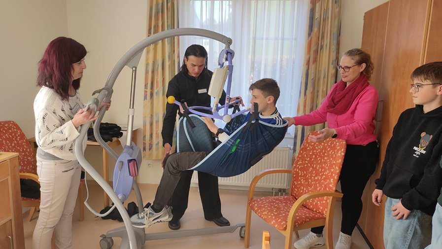 Beim Schnuppertag im ProCurand Seniorenzentrum Am Herzogschloss erlebte ein Schüler mit einem speziellen Hilfsmittel, wie es sich anfühlt, von Pflegekräften unterstützt zu werden, während er in die Rolle eines älteren Menschen schlüpfte.