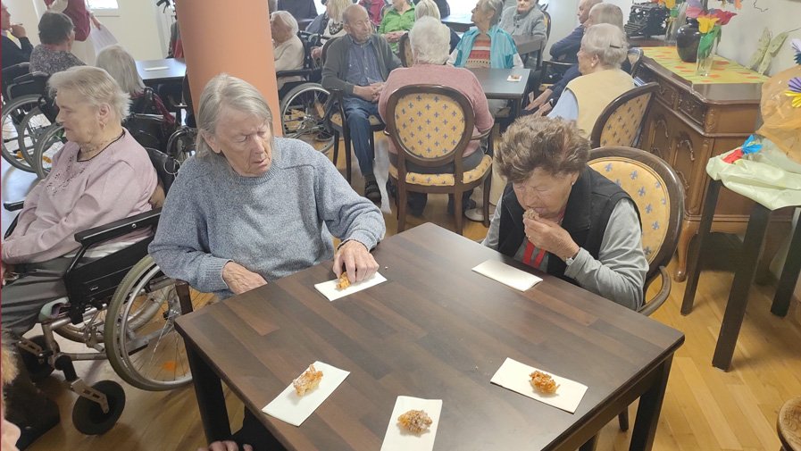 Die Senior*innen genießen ihre frisch gebackenen Hollerküchln in der Cafeteria des ProCurand Seniorenzentrums Am Herzogschloss.